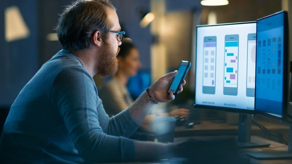 an image of a man engrossed in his phone, possibly searching for something and being targeted by an effective advertising strategy. the image conveys how businesses can use mobile marketing tactics to capture the attention of their target audience and engage them with their brand.