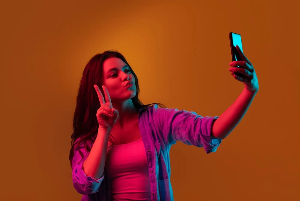 an image of a woman holding a phone, as if taking a selfie. the image is used to illustrate the importance of avoiding vanity metrics in digital marketing. vanity metrics, such as the number of likes or followers, may provide a sense of validation, but they do not necessarily translate to business success. instead, businesses should focus on meaningful metrics, such as engagement rates, conversion rates, and revenue generated.