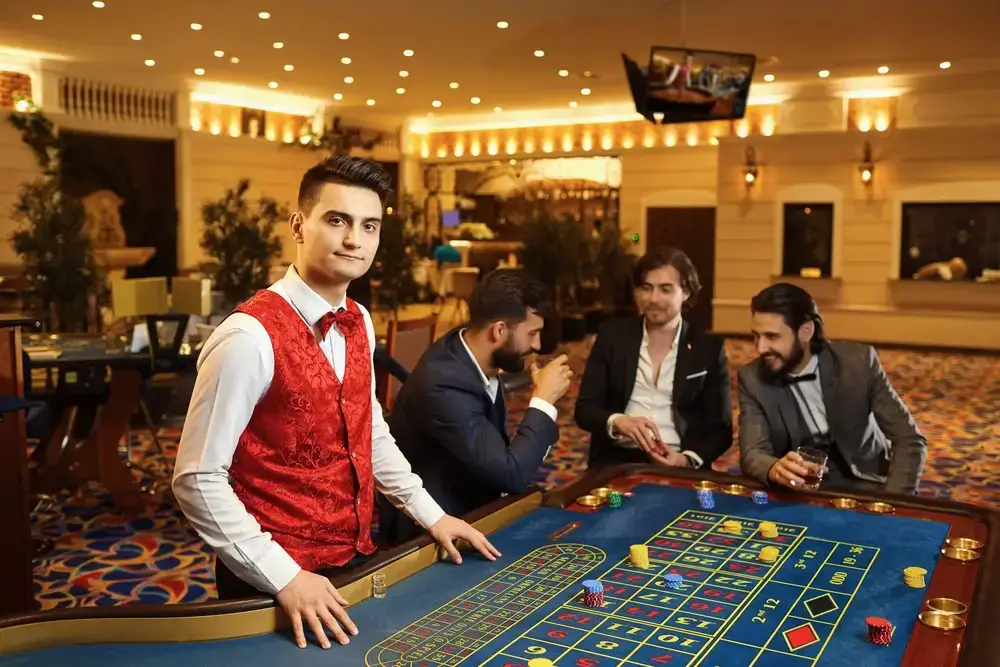 A casino dealer in a red vest stands at a roulette table as three men gamble, illustrating the illusion of control bias.