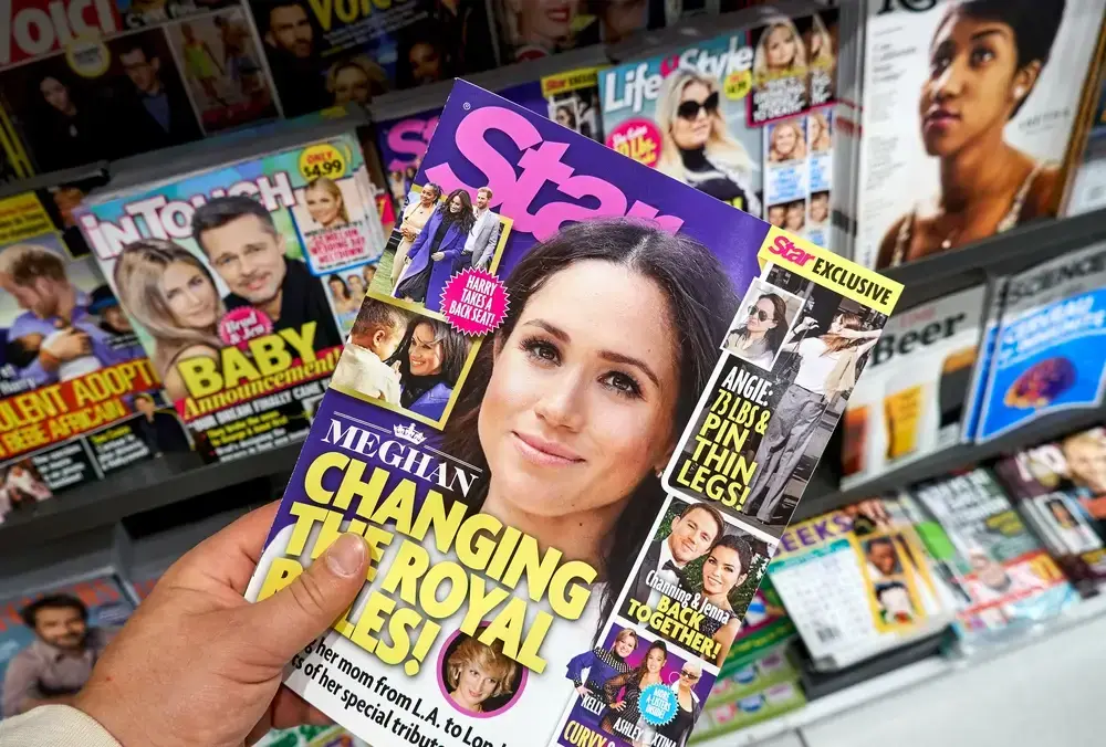 A hand holds a Star magazine featuring Meghan Markle, surrounded by other celebrity magazines. This illustrates the importance of choosing how many SEO keywords to use for impactful headlines.