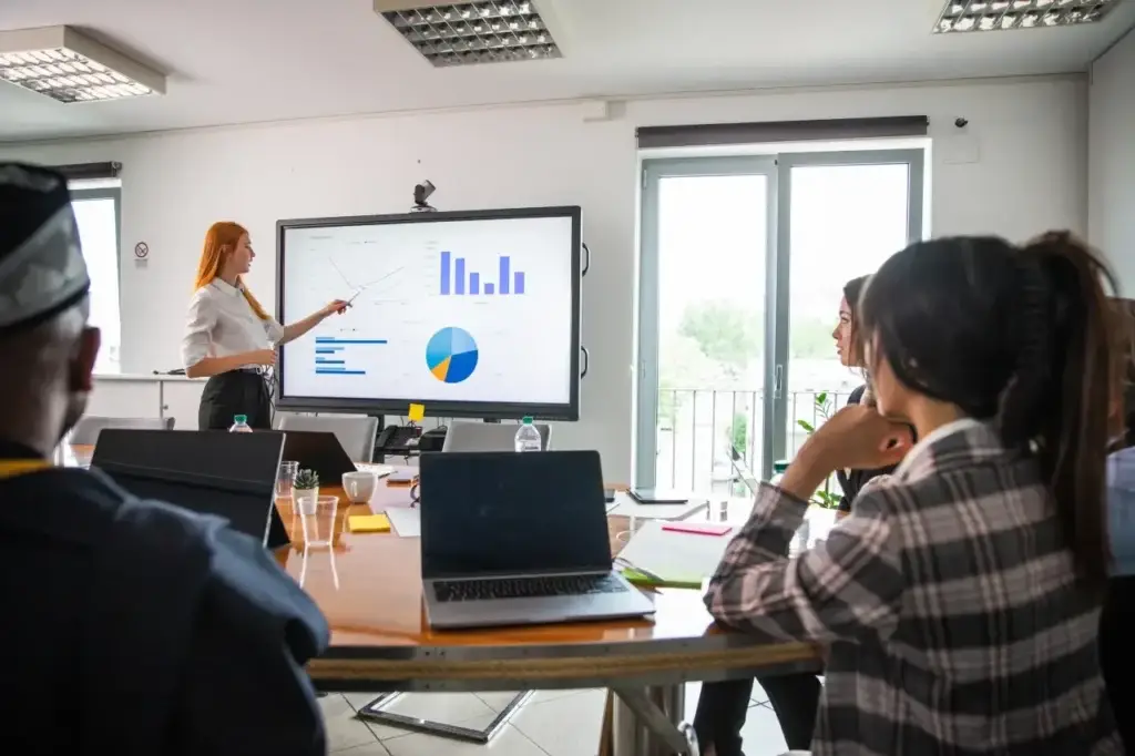 A businesswoman presents data graphs on a large screen to colleagues, discussing on page SEO services strategy.