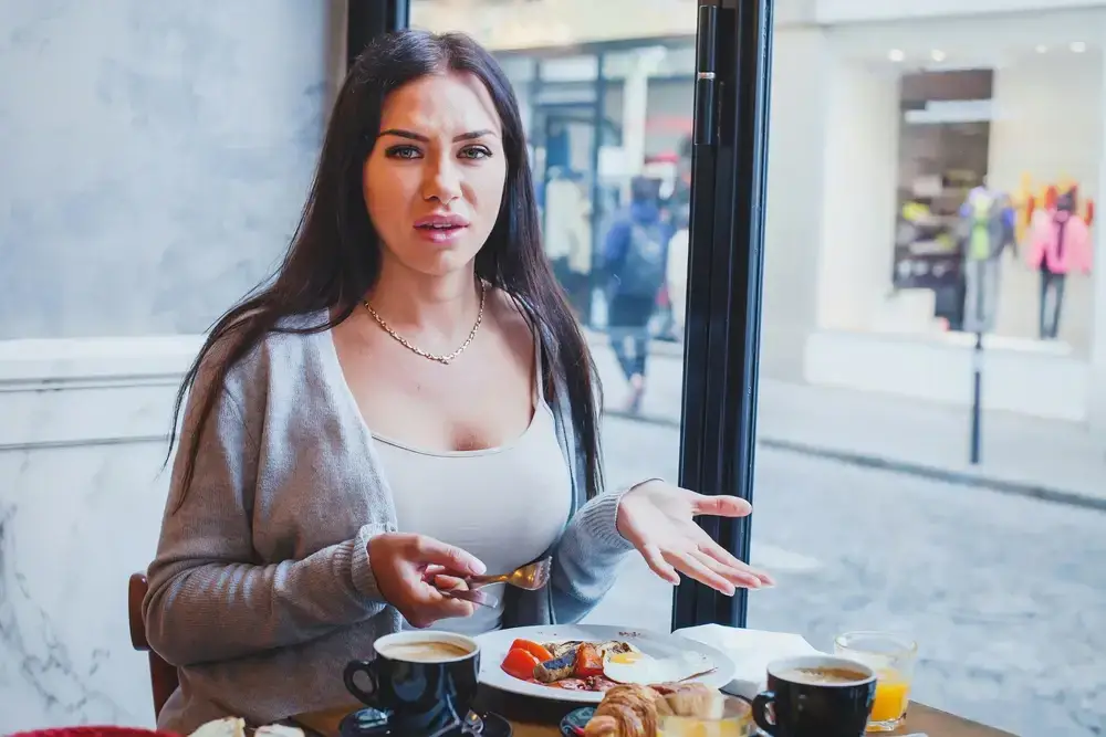 Woman looking displeased at a cafe table with breakfast, suggesting a poor customer experience that impacts how to increase customer lifetime value.