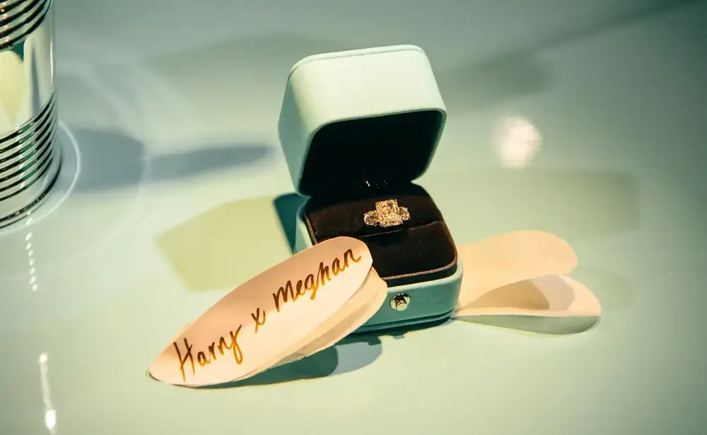 Diamond engagement ring in an open Tiffany blue box next to a white card with 'Harry x Meghan' written in gold, showcasing pricing psychology.