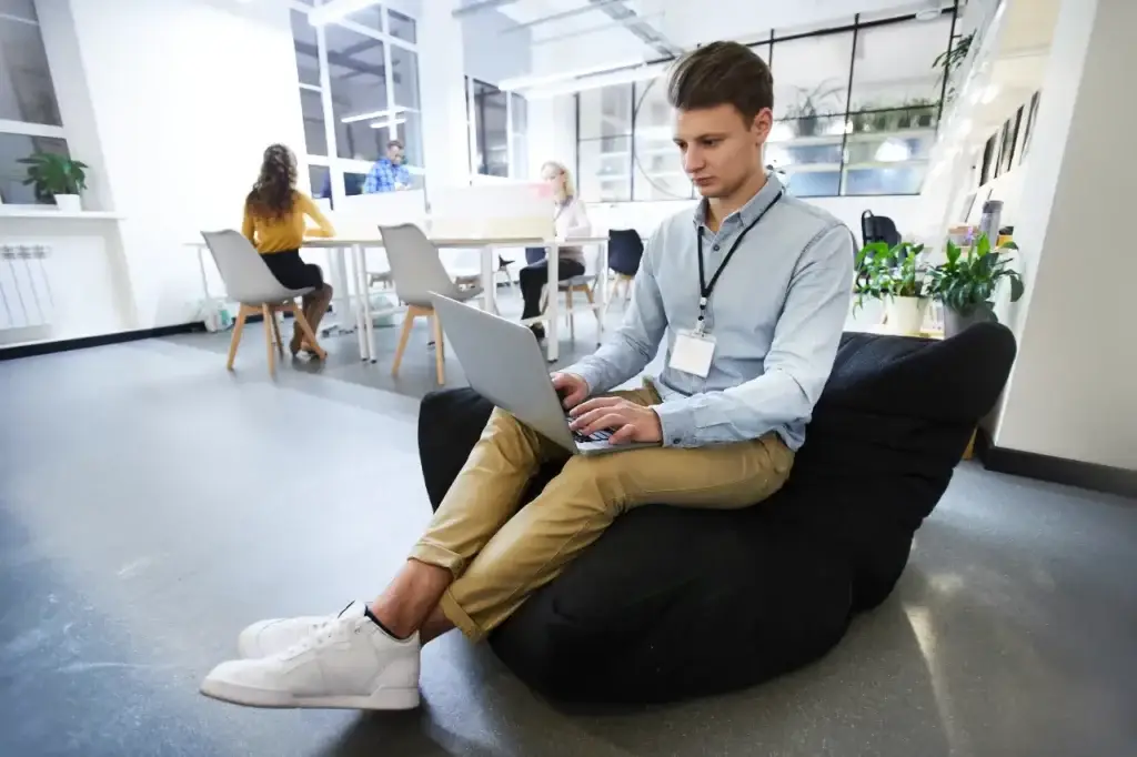 Man on a beanbag using a laptop, strategizing for a dental Google Ads agency campaign in a modern office.