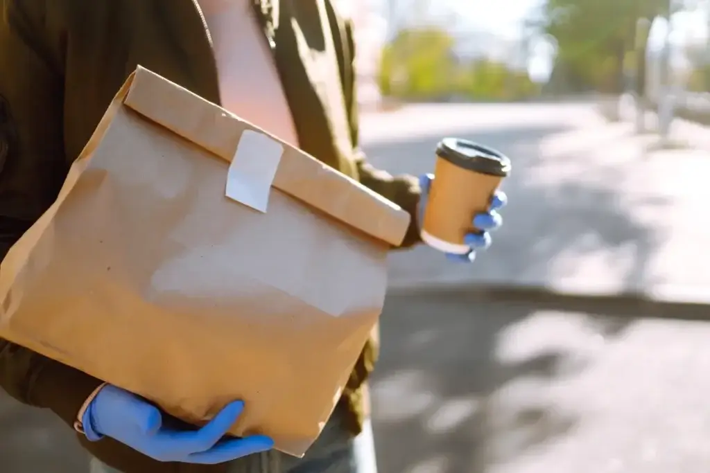 Person in blue gloves delivering a coffee cup and paper bag, a result of effective weather based marketing.