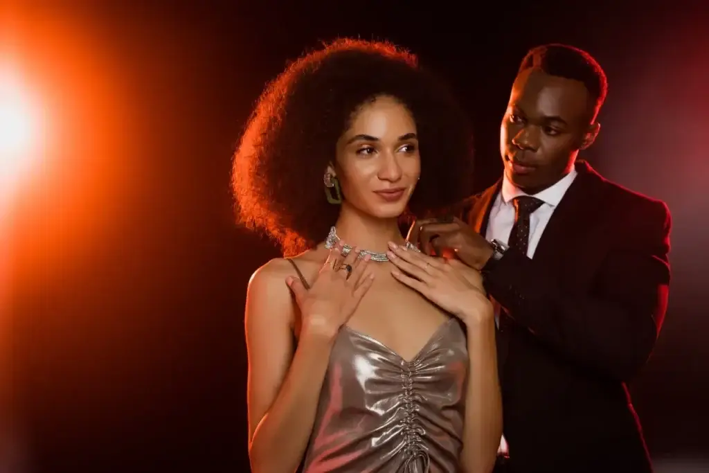 Man in suit fastening a sparkling necklace on a woman in a metallic dress, demonstrating self enhancement bias.