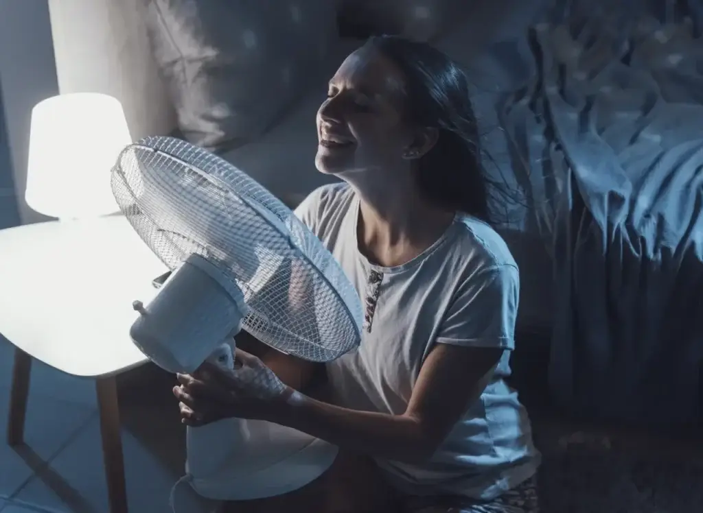 Woman smiling, enjoying cool air from a fan on a hot summer night, illustrating the impact of weather based marketing.