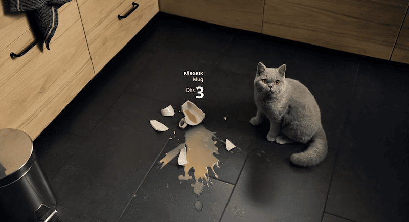 A British Shorthair cat sits next to a broken mug and spilled coffee on a kitchen floor, an example of emotional marketing.